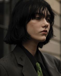 a man with black hair wearing a suit and green neck tie in front of a building