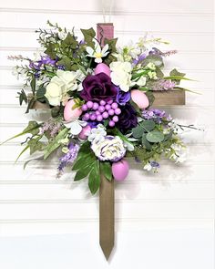 a cross decorated with flowers and greenery hanging on the side of a white wall