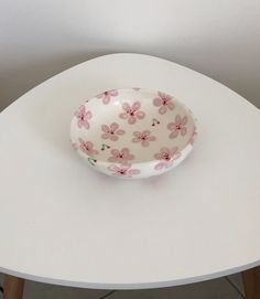 a bowl sitting on top of a white table next to a wooden leg vase with pink flowers