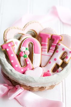 a basket filled with lots of pink and white decorated cookies in the shape of letters