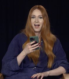 a woman with long red hair is holding a cell phone in her hand and laughing