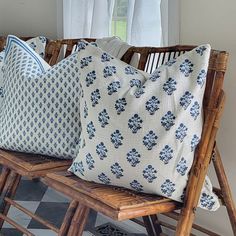 three decorative pillows sitting on top of a wooden bench next to a window with white curtains