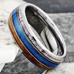 two wedding bands with blue and brown wood inlays are on top of each other