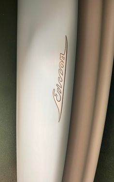 closeup of the side of a white surfboard with brown lettering on it and an orange stripe