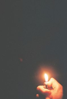 a person holding a small lit candle in their left hand, against a dark background