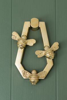 a brass door handle with two bees on it's side, attached to a green painted wall