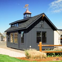 a small gray building with a clock tower on top and a wooden fence around it