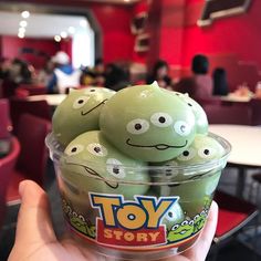 a person holding up a plastic cup filled with toy story green eggs in a restaurant