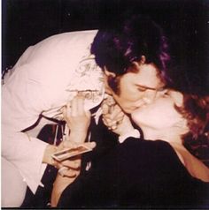 a man and woman kissing each other while holding wine glasses