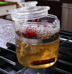 a glass jar filled with liquid sitting on top of a stove burner covered in ice and strawberries