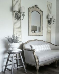 a white couch sitting next to a wooden stool in a living room under two mirrors