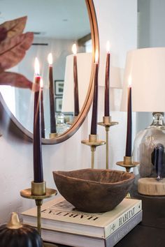 a table topped with candles and a bowl on top of a book next to a mirror