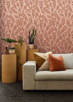 a white couch sitting in front of a pink wallpapered with leaves and plants