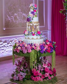 a multi - tiered wedding cake with pink and purple flowers on the top is surrounded by greenery