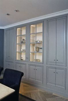 an empty dining room table and chairs in front of gray cupboards with glass doors