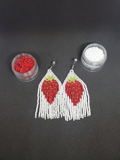 two red and white beaded earrings next to a container of beads on a black surface