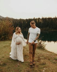 a man and woman holding hands while standing next to a lake