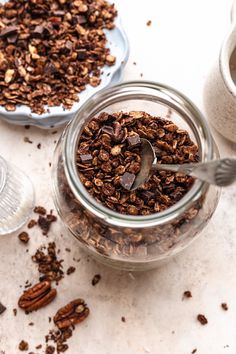 a glass jar filled with granola next to a bowl of pecans and a cup of coffee