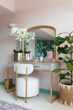 a vanity with a mirror, stool and potted plant