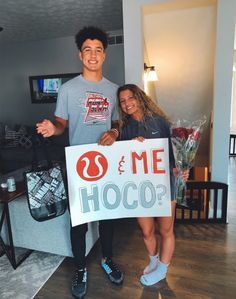 a man and woman standing next to each other holding a sign that says hoco?