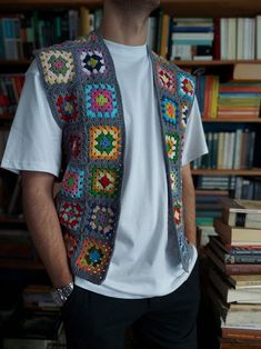 a man standing in front of a bookshelf wearing a crocheted vest