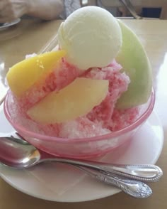 a bowl filled with ice cream and fruit on top of a plate next to a spoon