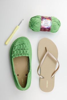 a pair of green slippers next to a ball of yarn and crochet hook