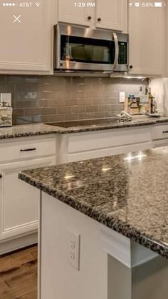 a kitchen with white cabinets and granite counter tops in front of a stainless steel microwave