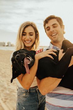 a man and woman holding a dog on the beach