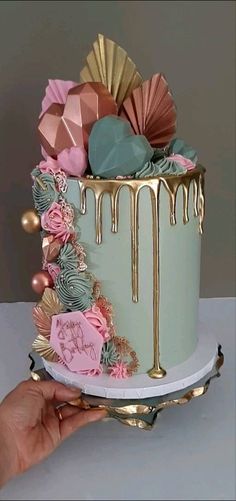 a hand is holding a cake decorated with flowers and icing on a white table