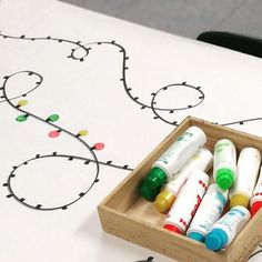 several markers in a wooden box on a table with christmas lights drawn on the background