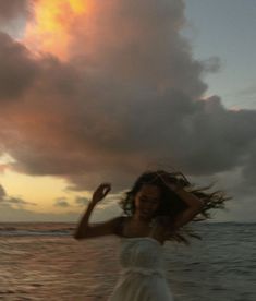 a woman in a white dress is standing on the beach with her hair blowing in the wind