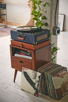 a record player sitting on top of a wooden table next to records and cds in front of a plant