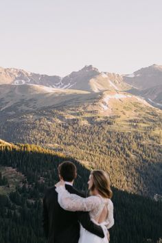 a bride and groom standing on top of a mountain