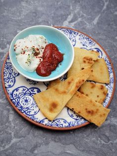 a blue and white plate topped with pita bread next to a bowl of yogurt