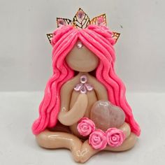 a small figurine with pink hair sitting on the ground holding a heart shaped rock