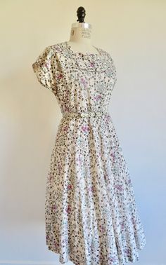 "This dress is made in the prettiest fabric. Made in the late 1940's to early 50's. Ivory/bone rayon eyelet in a floral print of magenta/pink and aqua blue with black outlines. Bodice has a squarish neckline with pretty pleat trim just beneath the front opening. as well as short capped sleeves. Set in waist has a fabric belt. Full skirt falls to the mid calf. Unlined. Side zipper closure. Label: None. I believe the dress was custom made. Professional construction. Condition: Excellent. The hemli Fitted Cream Vintage Dress With Floral Print, Beige Floral Print Vintage Dress, Beige Vintage Dress With Floral Print, Beige Floral Vintage Dress, Vintage Floral Print Dress For Tea Party, Cream Vintage Dress For Spring Garden Party, Vintage Dress For Garden Party, Vintage White Cottagecore Dress For Garden Party, Cottagecore Vintage White Dress For Garden Party