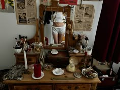 a dresser with a mirror and various items on it in front of a woman's reflection