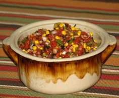 a bowl filled with corn and salsa on top of a striped table cloth next to a wooden spoon