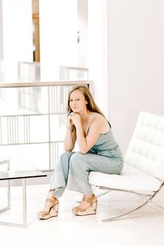 a woman is sitting on a white chair in the middle of a room with a glass table