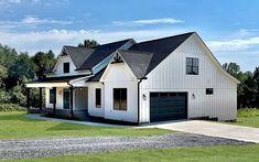 a white house with black roof and two car garages on the side of it