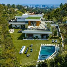 an aerial view of a house with a swimming pool in the foreground and trees surrounding it