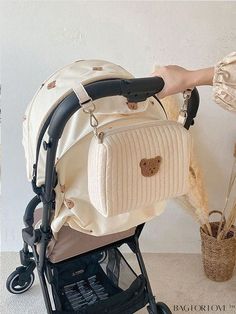 a baby stroller with a teddy bear on the handlebars, in front of a white wall