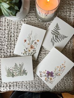 four cards with pressed flowers on them next to a candle