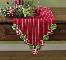 a red table cloth with green and white decorations sits on top of a wooden bench