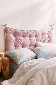 a bed with pink headboard and pillows on it next to a night stand that has a lit candle in front of it