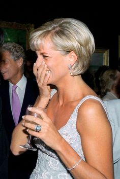 a woman laughing while holding a wine glass in her hand and another man standing next to her