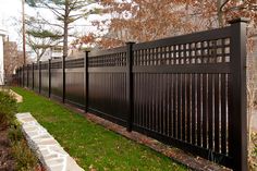 a black fence in front of a house with green grass and trees around the perimeter