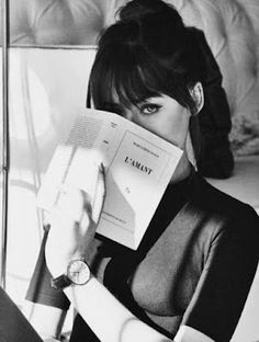 a black and white photo of a woman holding a book in front of her face