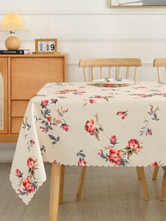 a dining room table covered with a flowered tablecloth and chairs in front of a dresser